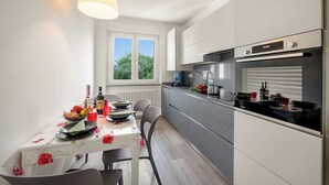 Et moderne køkken med hvide skabe, en indbygget ovn og et vindue der lukker naturligt lys ind.