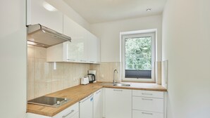 A compact kitchen with white cabinets, a wooden countertop, a built-in dishwasher, and a window with a view of greenery. - Apartamenty Swinoujscie- Sienkiewicza 23 (Swinoujscie)