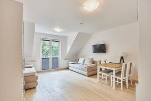 A modern living room with a sofa, a dining table, and a TV mounted on the wall. - Apartamenty Swinoujscie- Sienkiewicza 23 (Swinoujscie)
