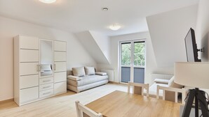 A modern, well-lit room with a loft-style ceiling, a large white wardrobe, a grey sofa, a wooden dining table, and a tripod-mounted camera. - Apartamenty Swinoujscie- Sienkiewicza 23 (Swinoujscie)