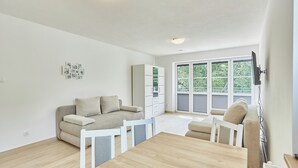 A modern living room with a sofa, a dining table, and a TV mounted on the wall. - Apartamenty Swinoujscie- Sienkiewicza 23 (Swinoujscie)