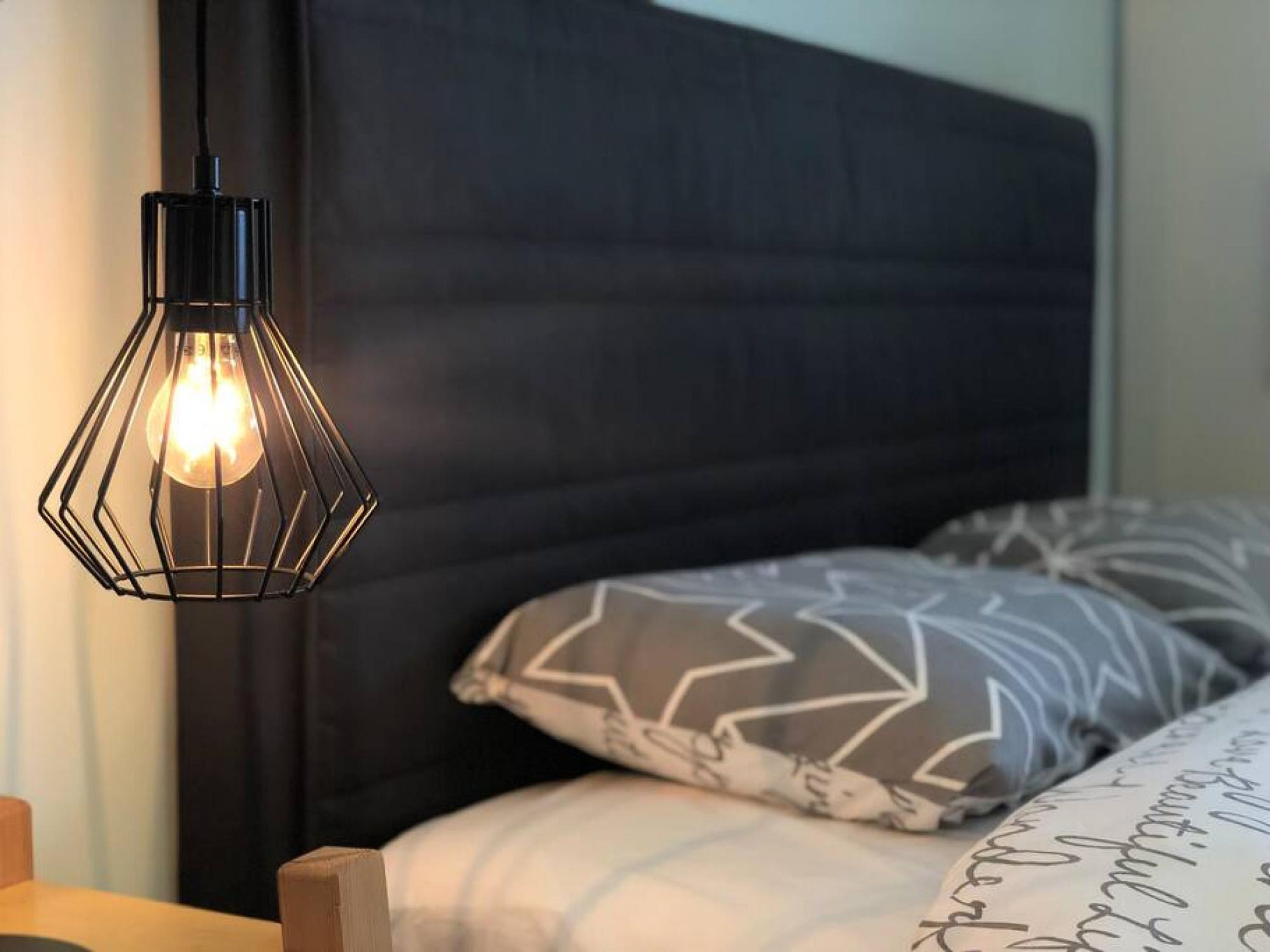 A bed with geometric patterned pillows, a dark headboard, and a hanging light fixture.