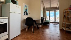 A modern kitchen with a white refrigerator, stove, and microwave. There is a dining area with a table and chairs, and a view of the outdoors through large windows. - View Lake Attic in Ioannina (Ioannina)
