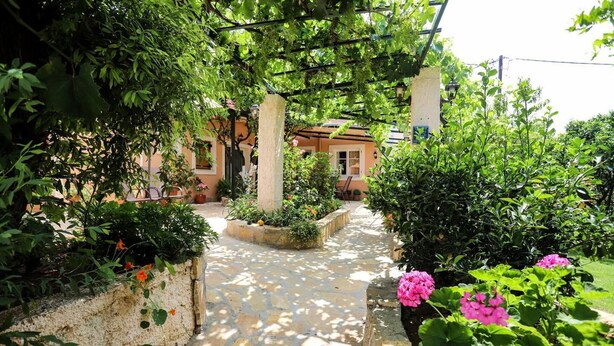 A stone pathway leading to a building with a garden area, surrounded by lush greenery and flowering plants. - Garden House Kastellani -corfu Greece Free Wi-fi (Corfu)