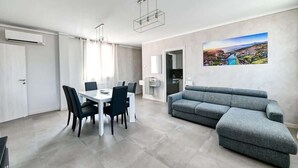 A modern living room with a grey sofa, a dining table with chairs, and a cityscape painting on the wall. - The Bridge - Peschiera Holiday (Peschiera del Garda)