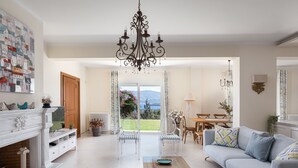 Un vaste salon doté d’une cheminée, d’un lustre et offrant une vue sur l’extérieur.