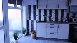 Una cocina moderna con armarios blancos, detalles de mármol negro, microondas integrado y plantas en macetas.