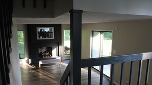 Een ruime woonkamer met een open haard, een trap en grote ramen.