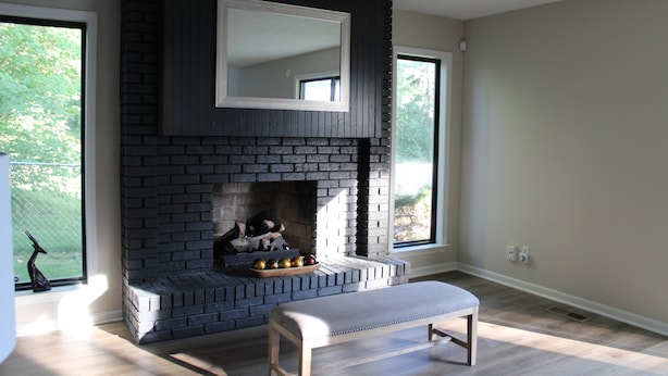Een moderne woonkamer met een metselstenen openhaard, een bank en grote ramen.