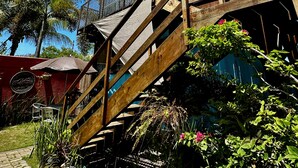 A wooden staircase leading to a balcony with a view of a garden and palm trees. - Pousada Contêiner 10 (Serra)