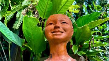 Una escultura de cabeza humana con expresión neutra, rodeada de abundante follaje verde.