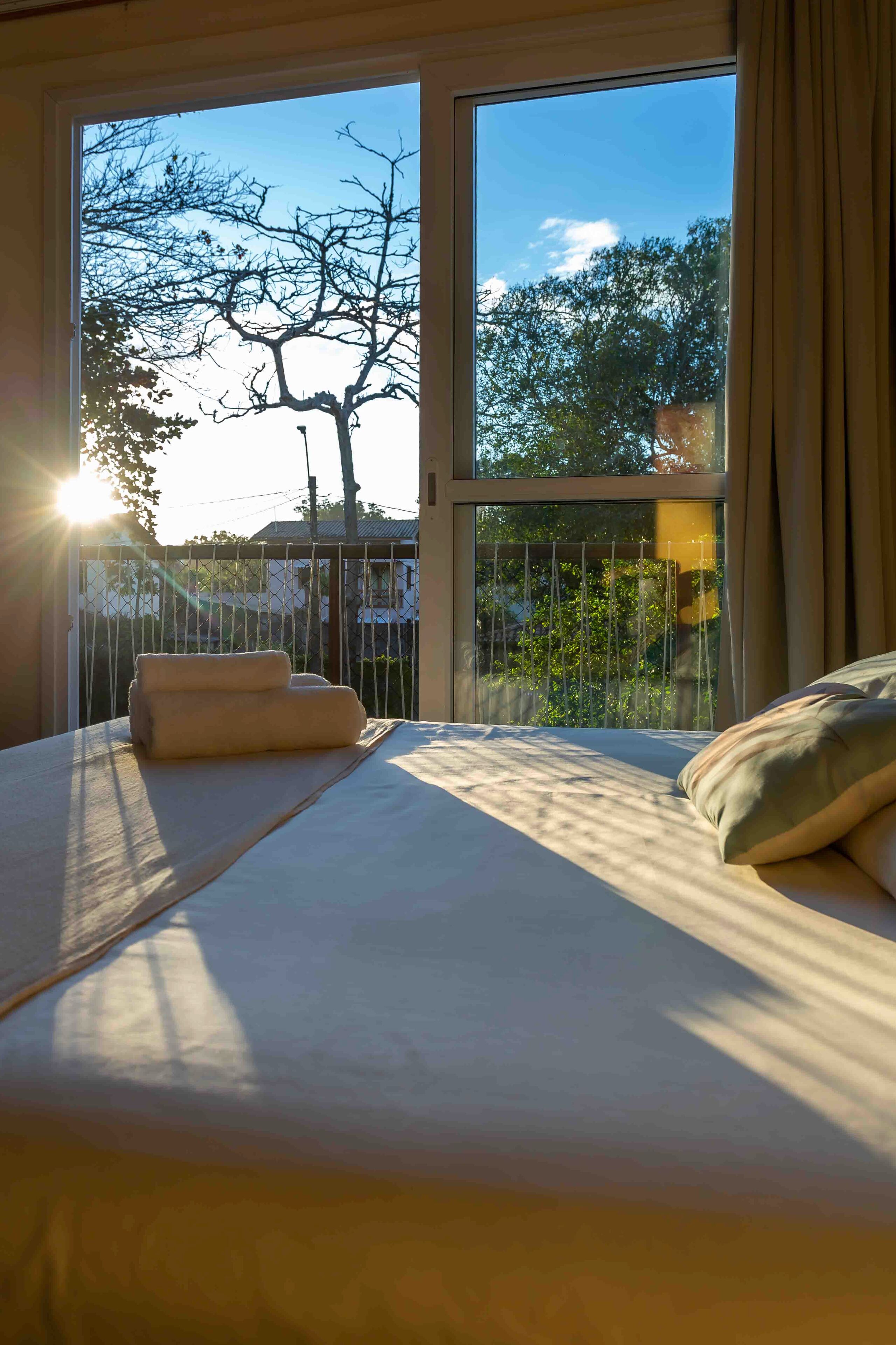 Un dormitorio con un ventanal grande, una cama y vistas a árboles y una valla.