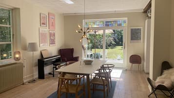 A dining area with a piano, a table with chairs, a lamp, and a view of the garden through the glass door.