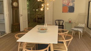 Un comedor con una mesa blanca, sillas de madera, una araña y un reloj.