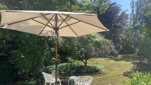 Un patio con una sombrilla beige, dos sillas blancas y una mesita.