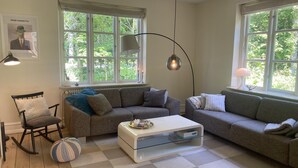 Una sala de estar con dos sofás, una mesita de centro, un sillón mecedora y un ventanal con vistas a la vegetación.