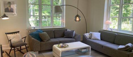 A living room with two sofas, a coffee table, a rocking chair, and a large window with a view of greenery.