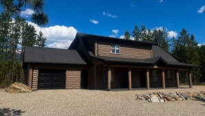 Une cabane en rondins à deux étages, dotée d’un garage, d’une véranda et d’une allée gravillonnée.