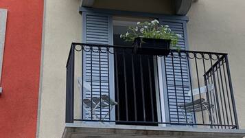 Un balcon avec une balustrade en métal noir, une petite table et un pot de fleurs.