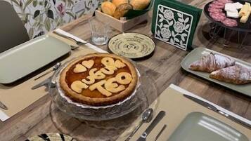 Una mesa de comedor dispuesta con platos, un pastel, un croissant y una hoja decorativa.