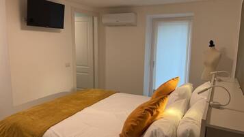 A hotel room with a bed, a television mounted on the wall, an air conditioning unit, a window with a view, and a mannequin head.