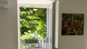 Een kamer met een deur die uitkomt op een balkon met uitzicht op geparkeerde auto's en groen.