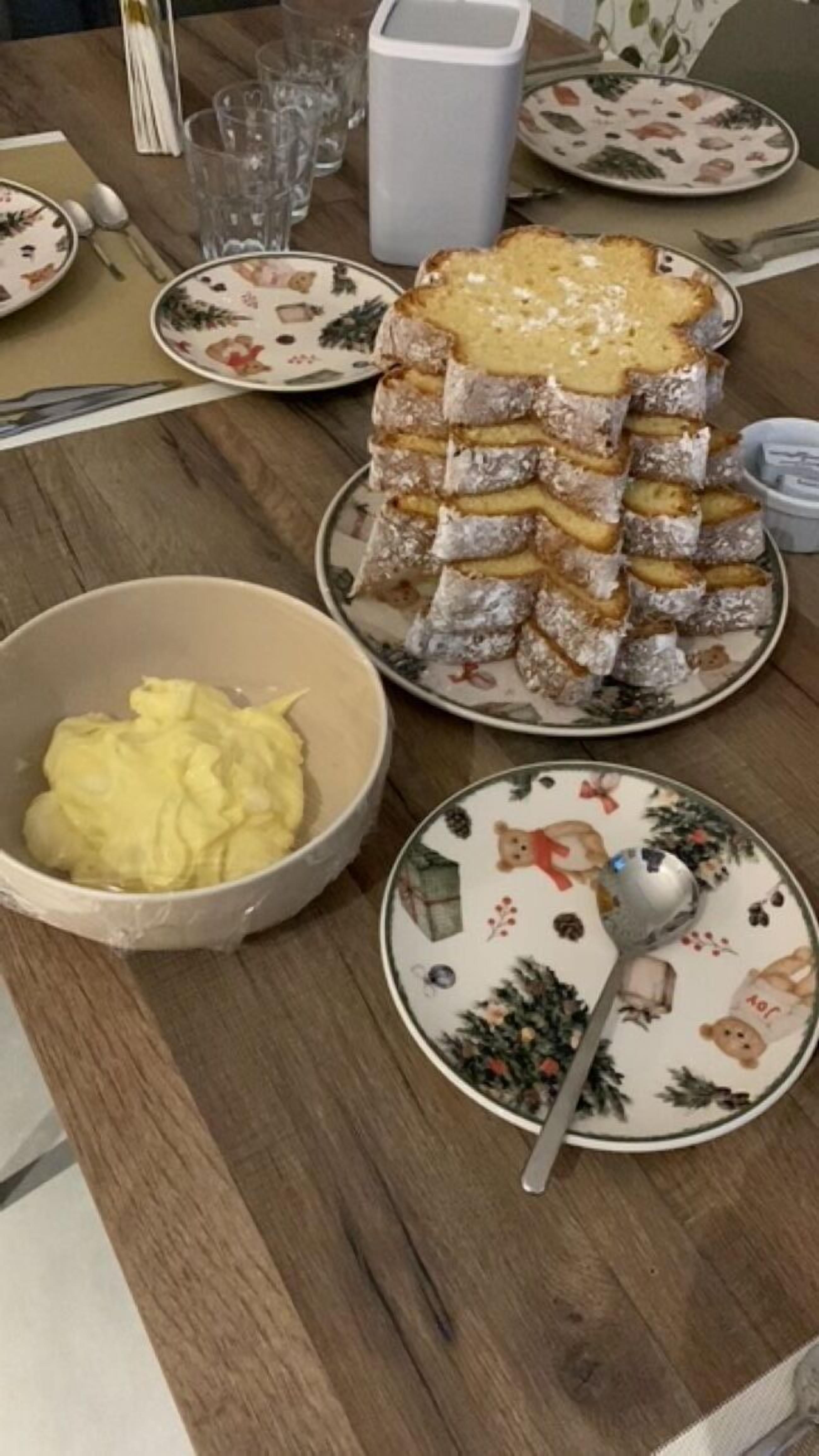 Una mesa de madera con un plato de pasteles en capas, un bol de crema amarilla y un plato con un diseño de oso.