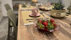 Een eettafel met een schaal aardbeien, een roze mok en een keramieken pot met een plant.