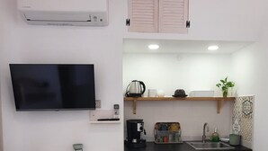 Uma cozinha compacta com geladeira embutida, cafeteira e pia. Há um pequeno espaço de jantar com duas cadeiras e uma mesa.