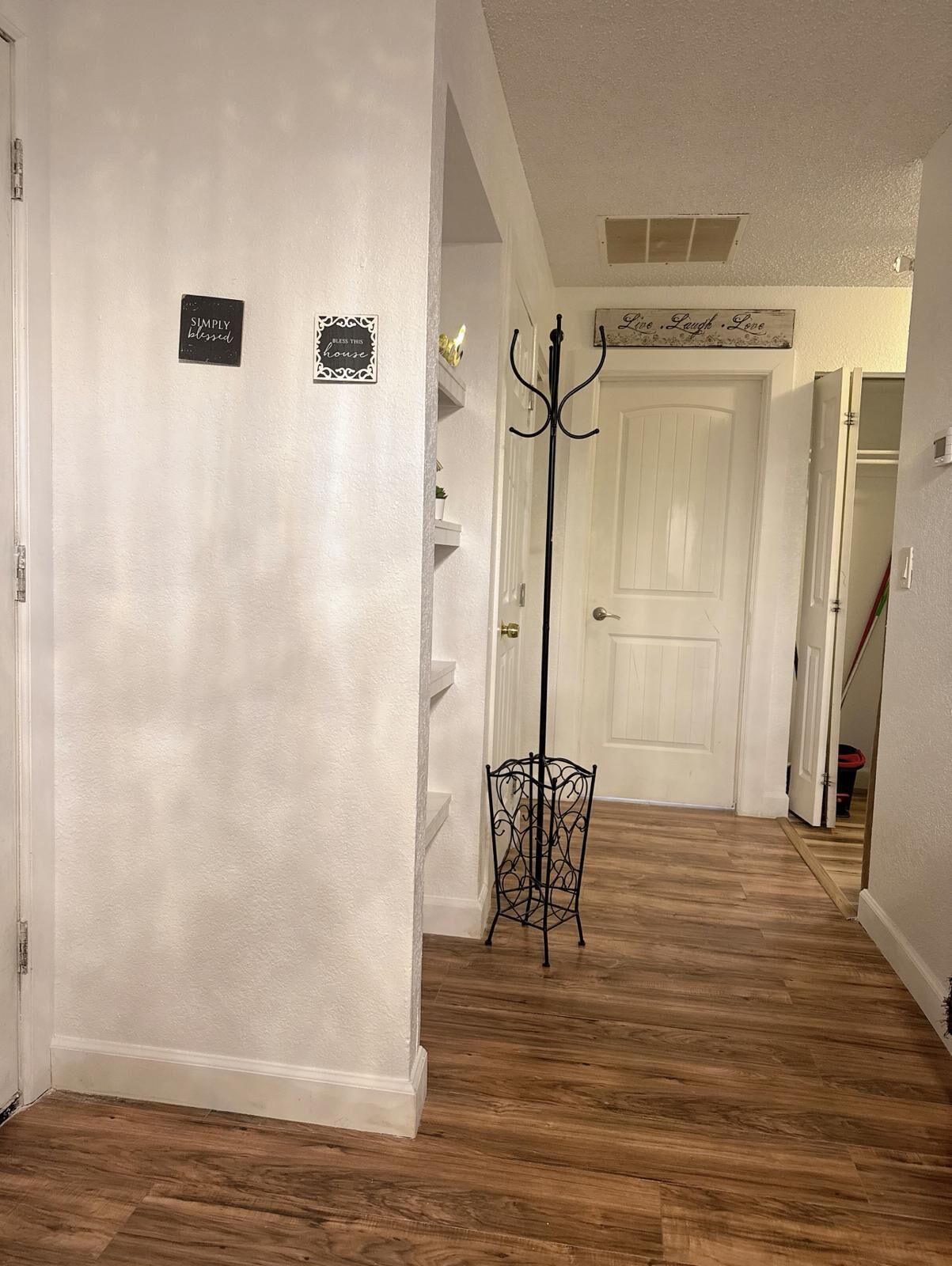 Un couloir aux murs blancs, avec un plancher en bois et un porte-manteau. On peut voir des panneaux sur le mur et une porte au fond.