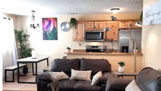 A modern living room with a dark leather sofa, a coffee table, and a kitchen area in the background.