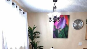 A small dining area with a table and benches, a potted plant, a painting, and a clock on the wall.