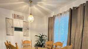 Une salle à manger avec une table et des chaises en bois, un luminaire suspendu et une plante.