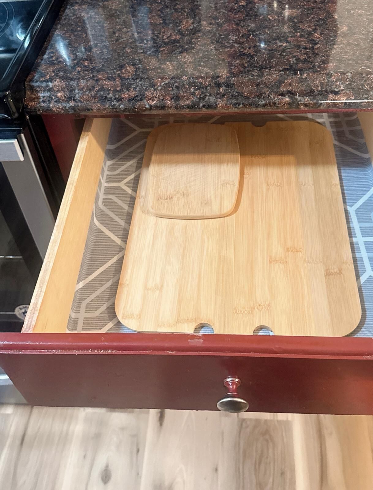 Un cajón de cocina con una tabla de cortar de madera y una encimera de granito arriba.