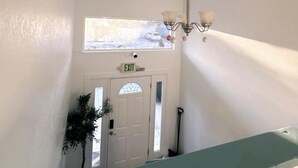 Un couloir avec une porte blanche, un panneau indiquant la sortie, un lustre et une fenêtre.