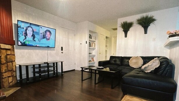 Un salon avec un canapé en cuir noir, une table basse en bois et un téléviseur fixé au mur.