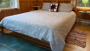 A bedroom with a bed, wooden headboard, two bedside tables with lamps, a ceiling fan, and a window with curtains. - Trailside Cottage #4 (Wreck Cove)
