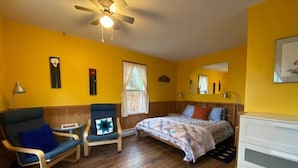 Quarto com cama, poltrona, escrivaninha, cômoda e ventilador de teto.