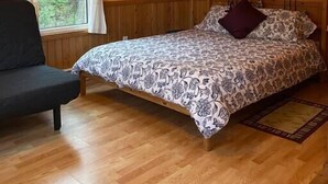 Ein Schlafzimmer mit einem hölzernen Bett, einem Sessel, einem Fenster mit Vorhängen und einem Spiegel an der Wand.
