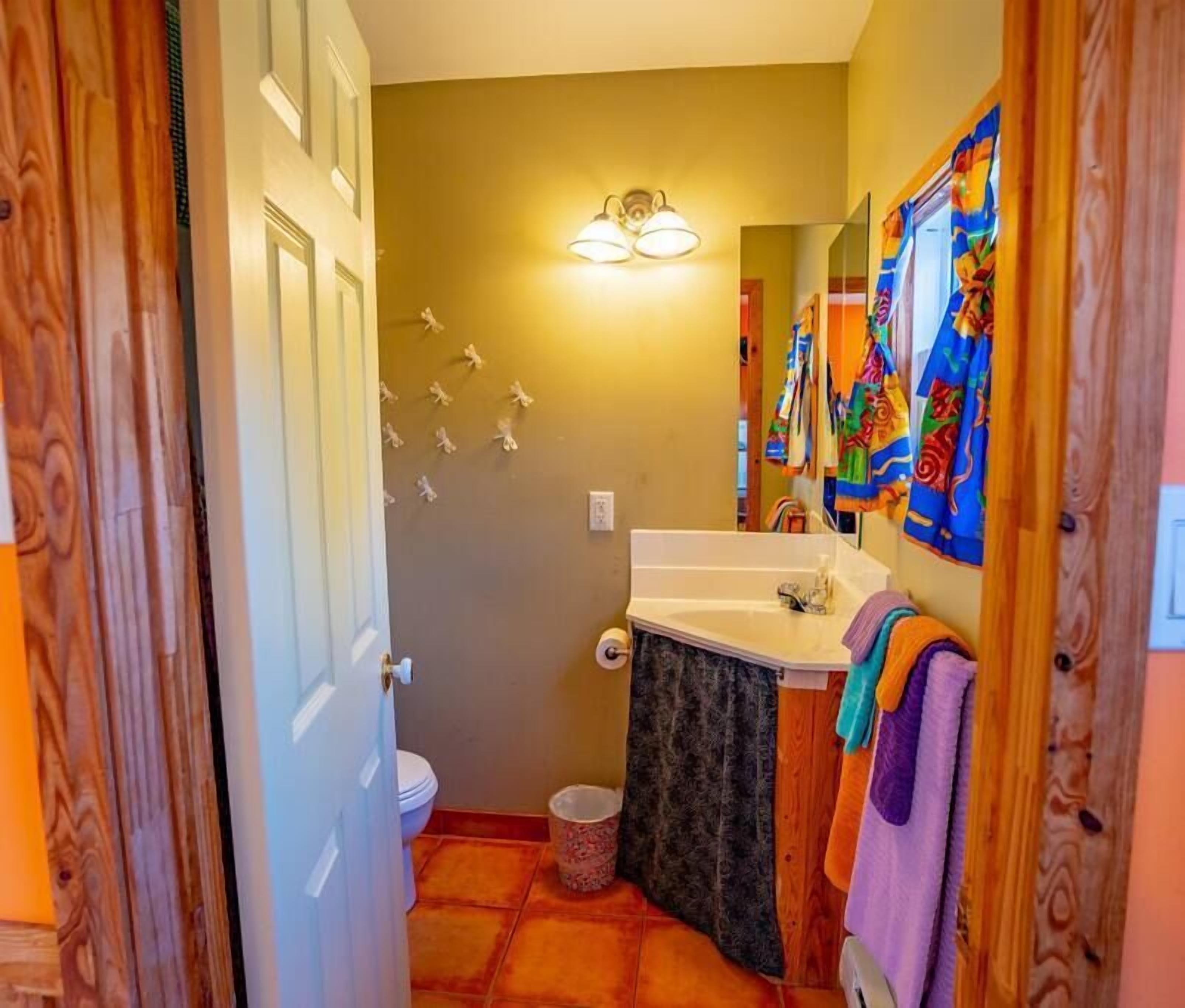 A bathroom with a white sink, a mirror, and a toilet. There are colorful towels hanging on the wall.