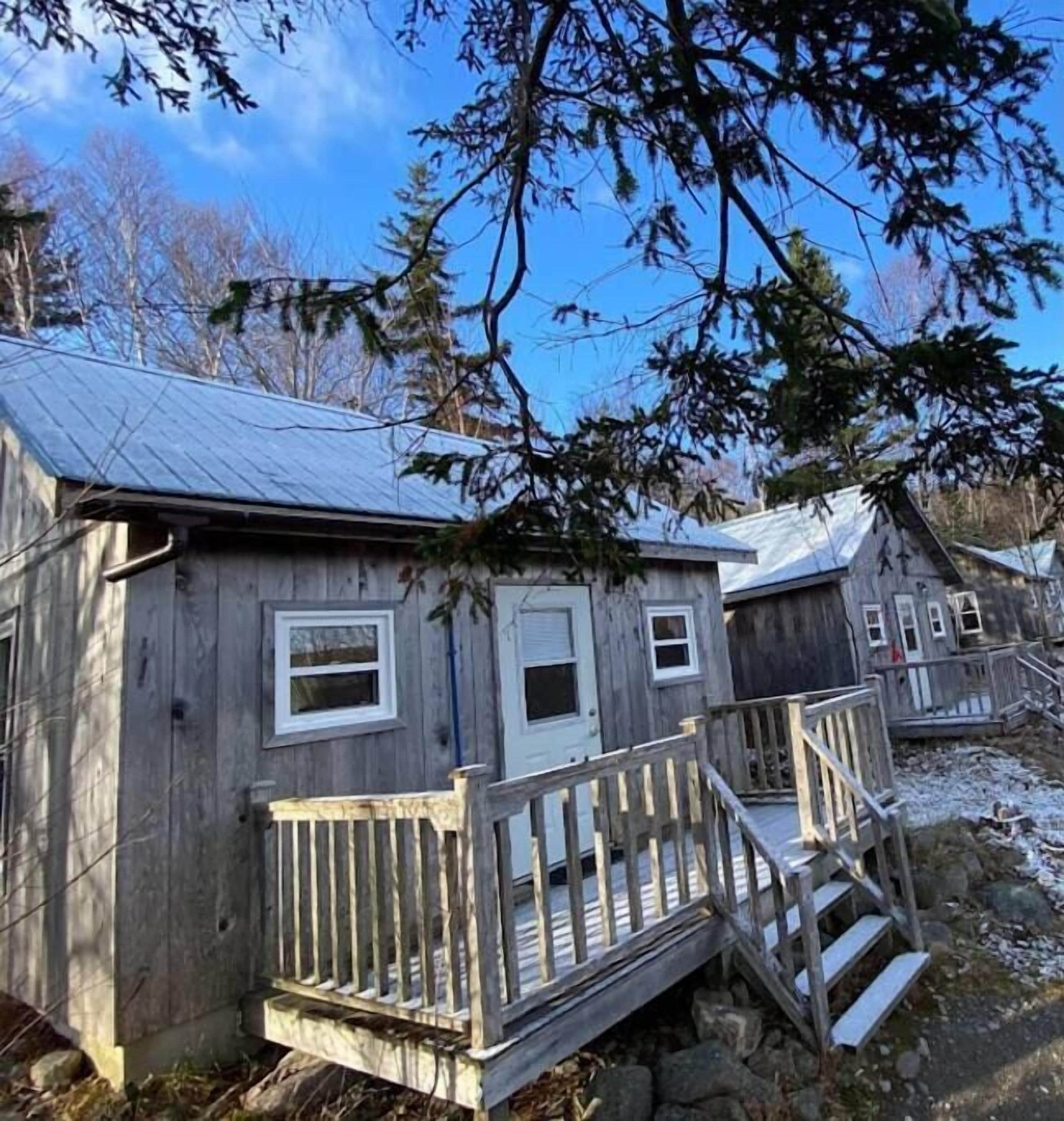 Une cabane en bois rustique, dotée d’un porche et d’un petit escalier menant à l’entrée.