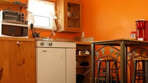 A compact kitchen with a white refrigerator, a microwave, and a stove. There is a wooden cabinet above the sink and a metal table with chairs. - Trailside Cottage #2 (Victoria County)