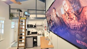 A modern kitchen with a built-in microwave, sink, and a small refrigerator. A wooden ladder leads to a loft area with a TV displaying a movie. - Charming Studio Loft In Hollywood Beach, Free Parking (Hollywood)