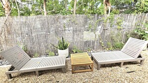 A covered outdoor seating area with two wooden lounge chairs and a small table, surrounded by pebbles and a bamboo fence. - Charming Studio Loft In Hollywood Beach, Free Parking (Hollywood)