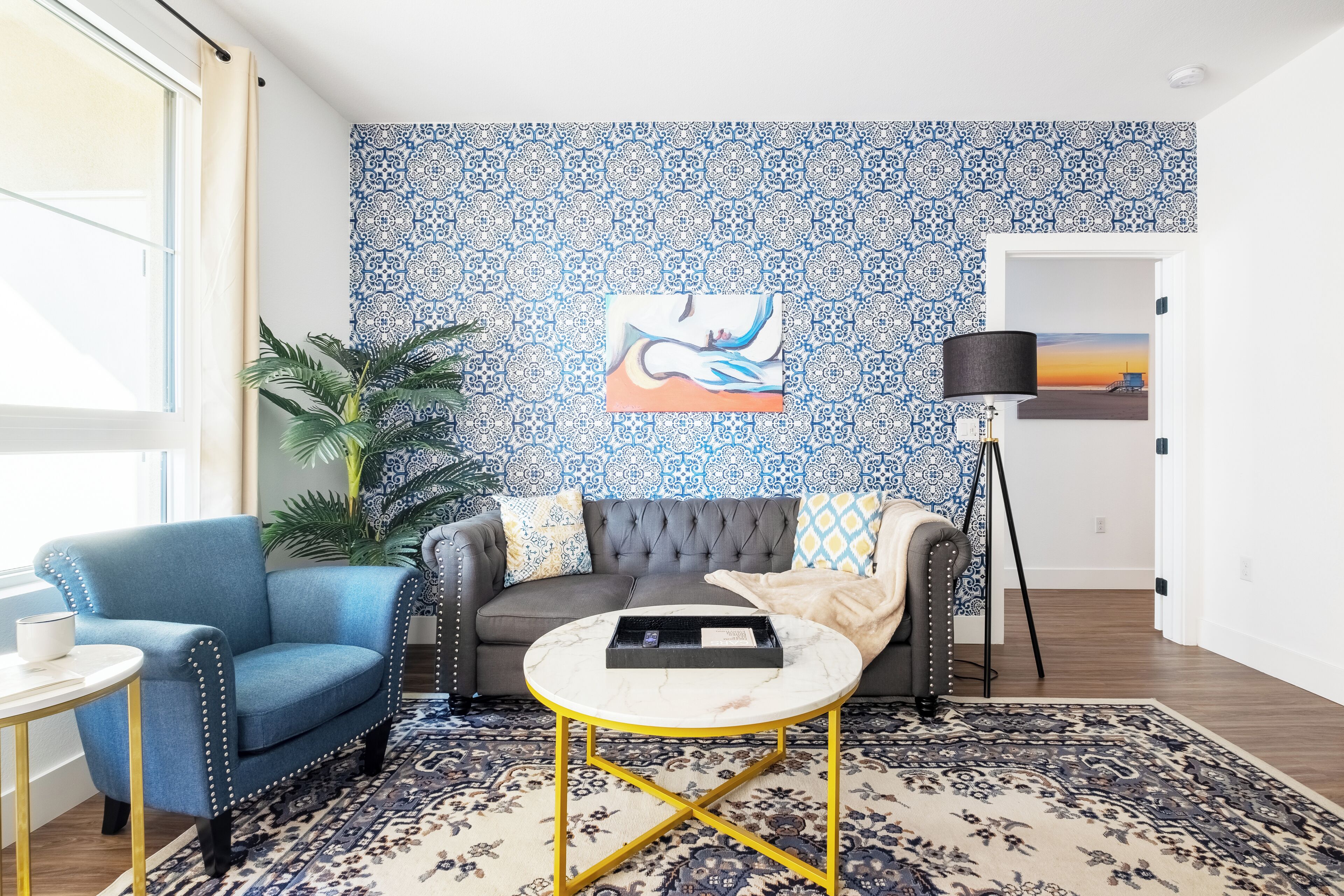 A living room with a patterned wall, a sofa, a blue armchair, a round coffee table, and a floor lamp.