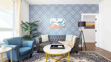 A living room with a patterned wall, a sofa, a blue armchair, a round coffee table, and a floor lamp.