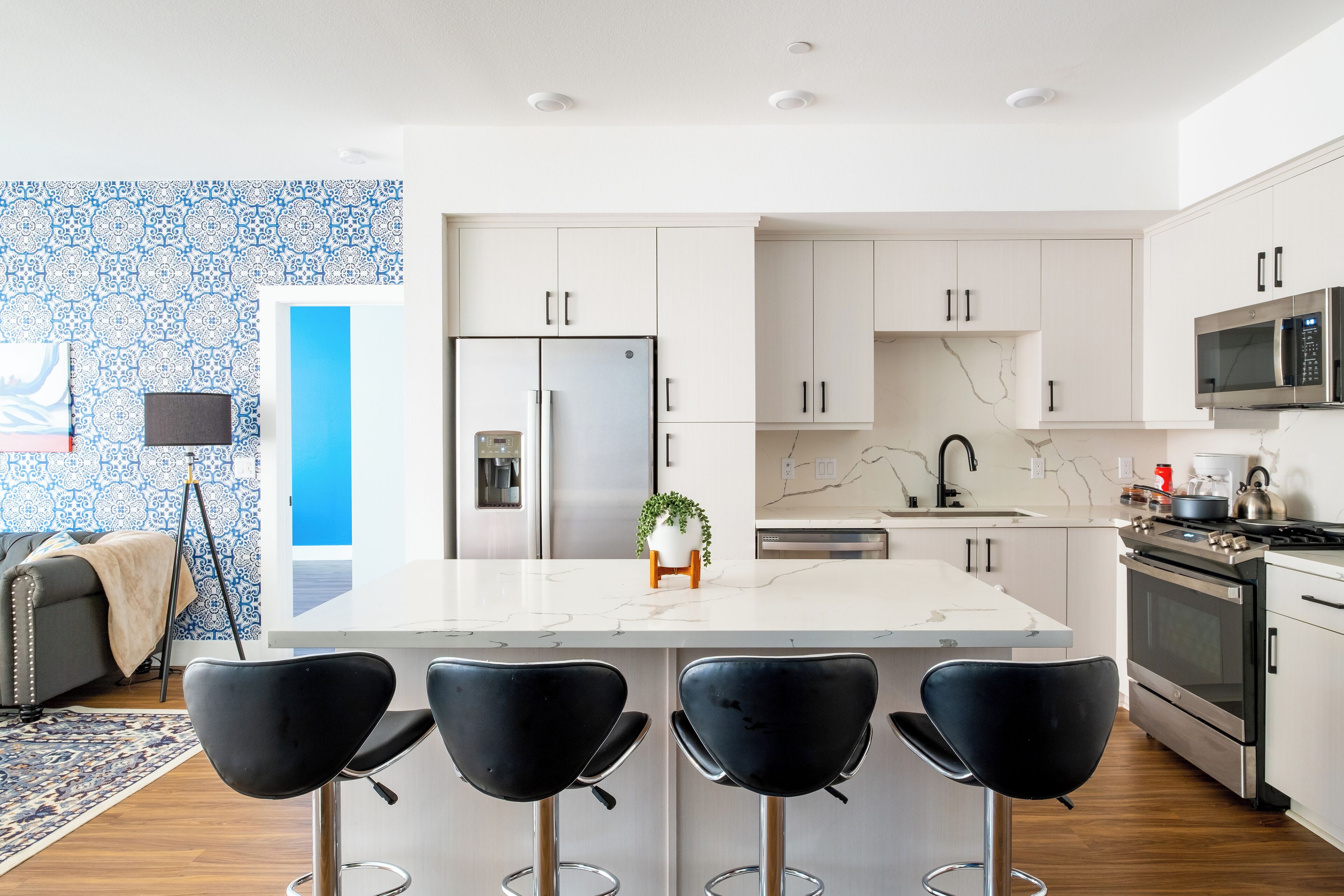 A modern kitchen with white cabinetry, a central island with bar stools, stainless steel appliances, and a patterned backsplash.