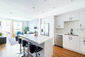 A modern kitchen with white cabinets, a central island with bar stools, a refrigerator, and a dishwasher. - Beach Condo 234CB (Carlsbad)