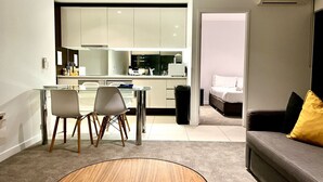 A modern living room with a grey sofa, a round wooden coffee table, and a dining area with a glass table and chairs. - Stunning City View 2BR in CBD by Readyset Apartments (Melbourne)