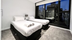 A modern hotel room with two beds, a large window with a city view, and a small bedside table with a lamp. - Stunning City View 2BR in CBD by Readyset Apartments (Melbourne)